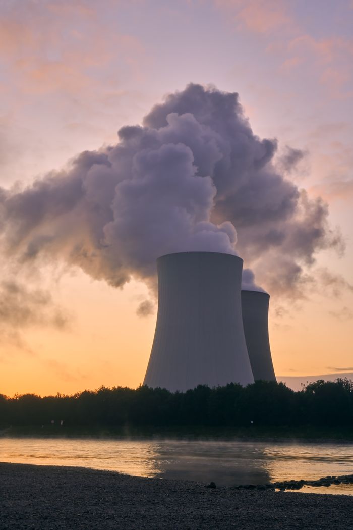 Silhouette of a nuclear power plant emitting steam during a colorful sunset.